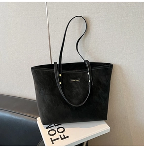 Detail of black suede tote bag with metal nameplate and gold rivet hardware accents