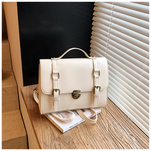 Close-up of vintage beige messenger bag with bronze buckle and leather texture on a wooden table
