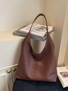 Dark brown large woven hobo shoulder bag in a minimalist home setting with warm lighting