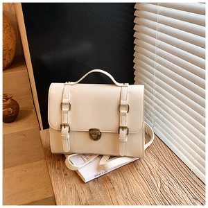 Detail shot of a cream white vintage messenger bag with bronze buckle on a wooden table