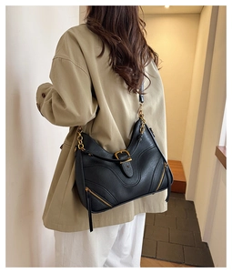 Detail der schwarzen Hobo-Tasche aus Leder mit goldener Hardware und einem beigen Trenchcoat