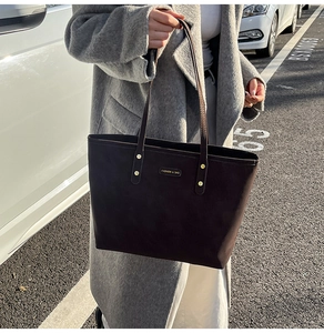 Detailed close-up of dark brown suede tote bag with gold metal logo and long shoulder straps