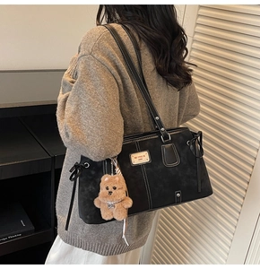 Detail of black suede tote bag with white stitching and plush bear charm on shoulder strap