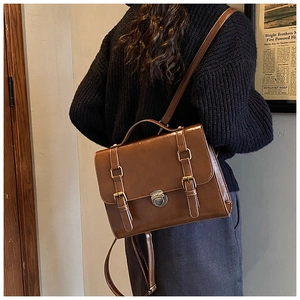 Detail of vintage brown leather satchel showing buckle straps and polished texture on model