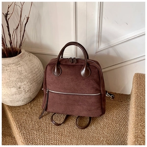 Détail d'un sac à dos en daim marron montrant la fermeture éclair et la texture mate