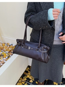 Détail du sac bandoulière vintage marron foncé avec boucle métallique sur un manteau d'hiver