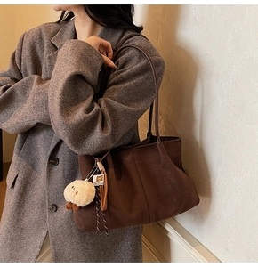 Detail of dark brown suede tote bag featuring a cute plush pendant and long shoulder strap