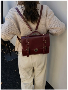 Outdoor back view of a model wearing a vintage dark red leather backpack on a beige sweater