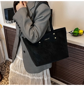 Side view of model wearing a black matte tote bag with round metal hardware detail