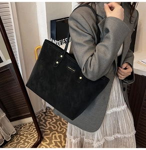 Close-up of black suede tote bag with golden hardware rivets and metallic fashion logo