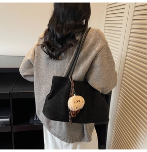 Detail of black suede tote bag with cream plush charm worn over a grey knit sweater
