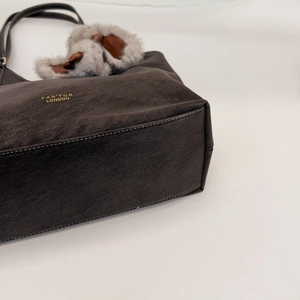 Detail view of dark brown leather tote bag with gold lettering and plush ball charm