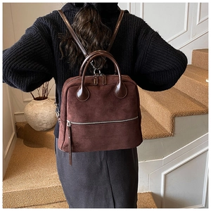 Sac à dos chic en daim marron foncé porté par un mannequin dans un décor intérieur