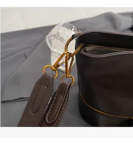 Gros plan sur les boucles dorées et la bandoulière en cuir grainé marron foncé du sac