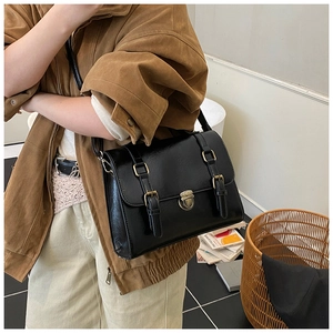 Close-up of vintage black glossy satchel with bronze metal lock and double buckle details