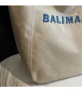 Detail of beige canvas tote bag featuring premium blue towel embroidery lettering