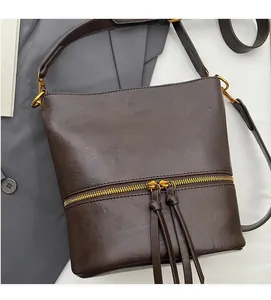 Gros plan détaillé du sac seau en cuir mat marron avec fermeture éclair dorée et franges