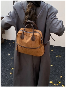 Détail d'un sac à dos en daim marron avec sangles foncées et doubles zips argentés
