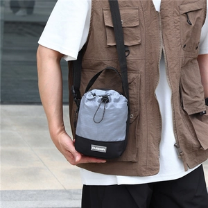 Detail van grijs en zwarte outdoor crossbodytas met trekkoord en modieus label