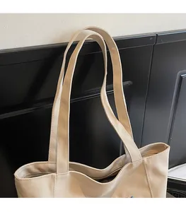 Close-up of beige canvas tote bag shoulder straps with blue letter embroidery detail