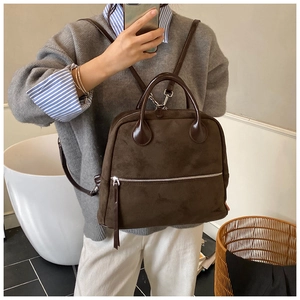 Détail du sac à dos en daim marron foncé avec poignée en cuir et zip métallique argenté