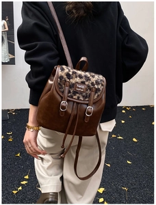 Dettaglio di uno zaino in pelle marrone scuro con patta in peluche leopardato e fibbie metalliche