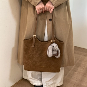 Brown suede tote bag detail featuring golden logo and cute white rabbit plush charm