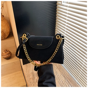 Détail du sac bandoulière noir avec chaîne dorée et rabat marqué sur fond rustique