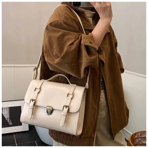 Detail view of cream messenger bag with bronze buckles and adjustable crossbody strap