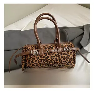 Detail of leopard print cylinder bag featuring brown leather straps and metal buckles