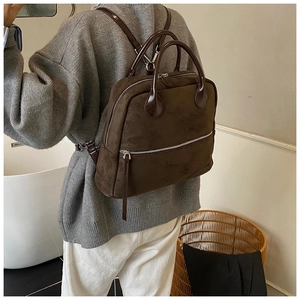 Détail du sac à dos en daim marron foncé avec fermetures éclair argentées porté