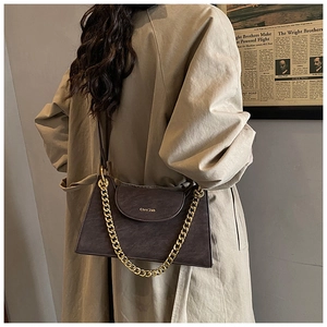 Détail d'un sac à main gris foncé à chaîne porté avec un trench-coat beige élégant