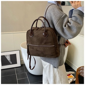 Détail d'un sac à dos en daim marron foncé avec fermetures éclair argentées et poignées