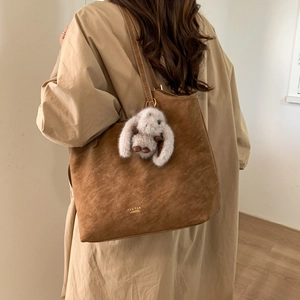 Brown suede tote bag with plush rabbit pendant shown as a shoulder bag on a model