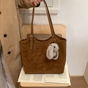 Detail of vintage brown leather tote bag with plush rabbit charm and gold logo on a chair