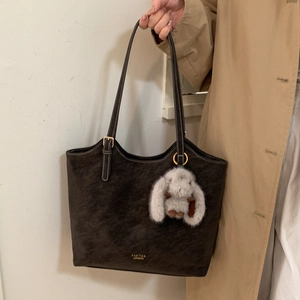 Detail of dark brown matte tote bag with gold logo and plush bunny charm accessory