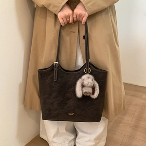 Detailed view of coffee brown suede tote bag with plush rabbit charm and gold logo