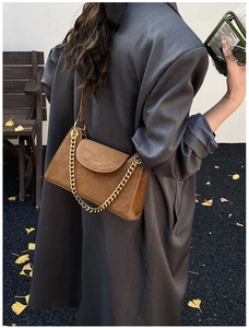 Détail d'un sac en daim marron avec chaîne dorée et logo de marque en style de rue
