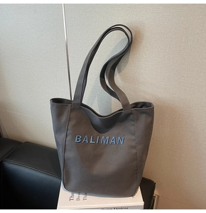 Close-up of dark grey canvas tote bag with blue embroidered logo on white books
