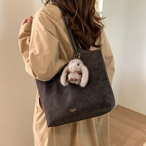 Detail of dark brown vintage tote bag with gold logo and plush rabbit charm