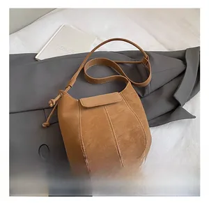 Detail showing the brown leather texture and vertical stitching of the crossbody bucket bag
