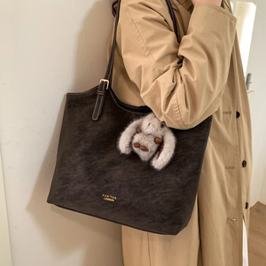 Detail of a dark coffee tote bag with a plush bunny charm and golden brand text