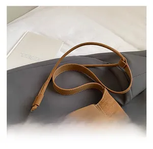 Detail view of brown leather bucket bag with contrast white stitching and adjustable strap
