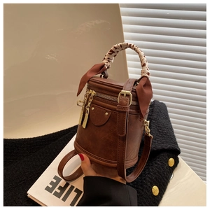 Detail of brown cylindrical handbag with leopard ribbon and golden hardware on tweed jacket