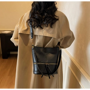 Détail d'un sac seau noir avec zip doré porté sur un mannequin en trench beige