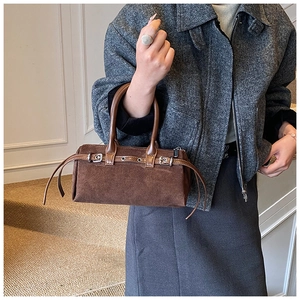 Brown suede pillow bag with vintage buckle straps shown in a minimalist interior setting