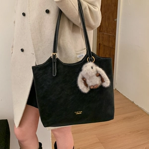Detail of black suede tote bag with white contrast stitching and plush bunny pendant