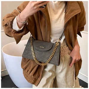 Détail d'un sac bandoulière en daim gris foncé avec chaîne dorée et logo de la marque