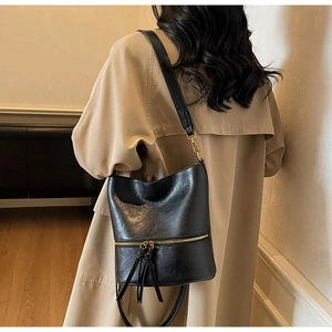 Détail du sac seau vintage en cuir noir avec fermeture éclair dorée et glands sur un manteau
