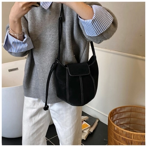 Detail of black suede bucket bag featuring contrast white stitching and leather strap
